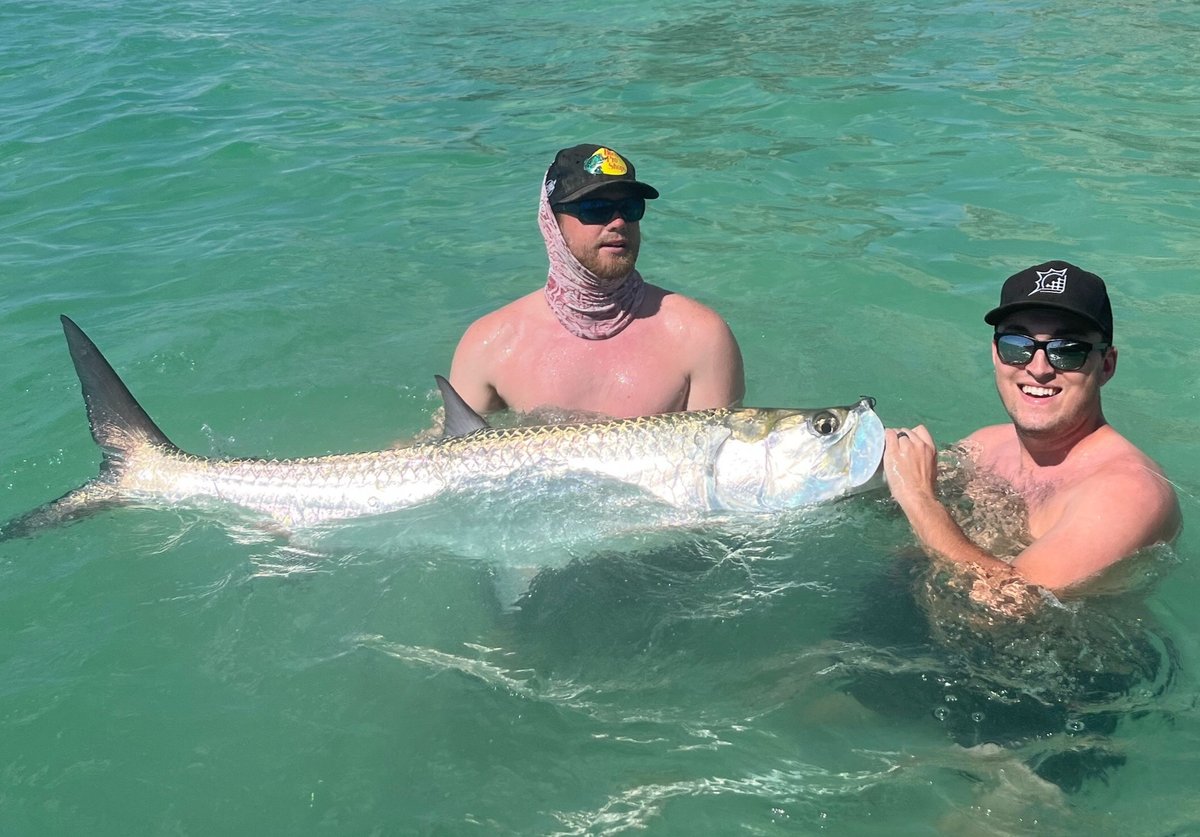 Two men holding a large Tarpon fish while standing in the ocean