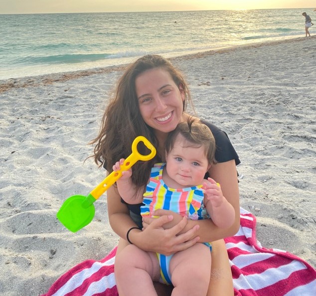 Mom holding her baby on the beach, sitting in the sand on a towel
