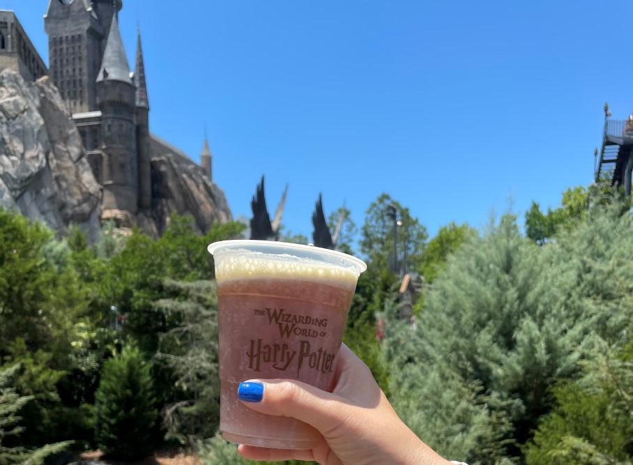 A woman's hand holding a cup from The Wizarding World of Harry Potter in front of the Hogwarts Castle