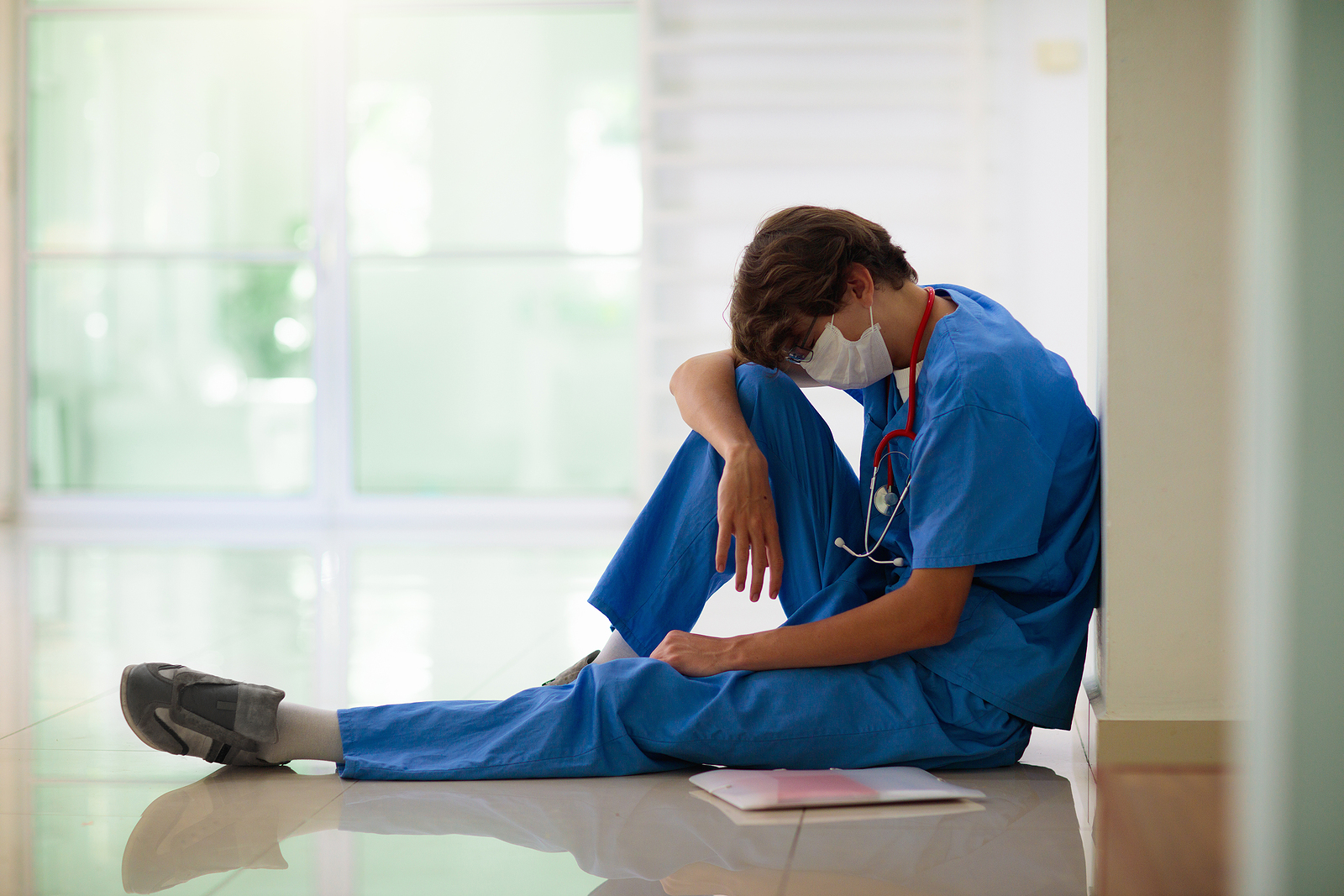 tired nurse sitting on floor with head on knee