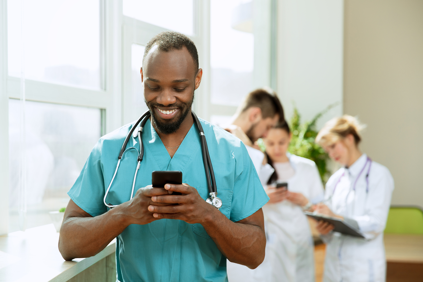 smiling african american male travel nurse with stethoscope around his neck holding phone